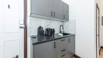 A compact kitchen with grey cabinets, a marble backsplash, and a black countertop.