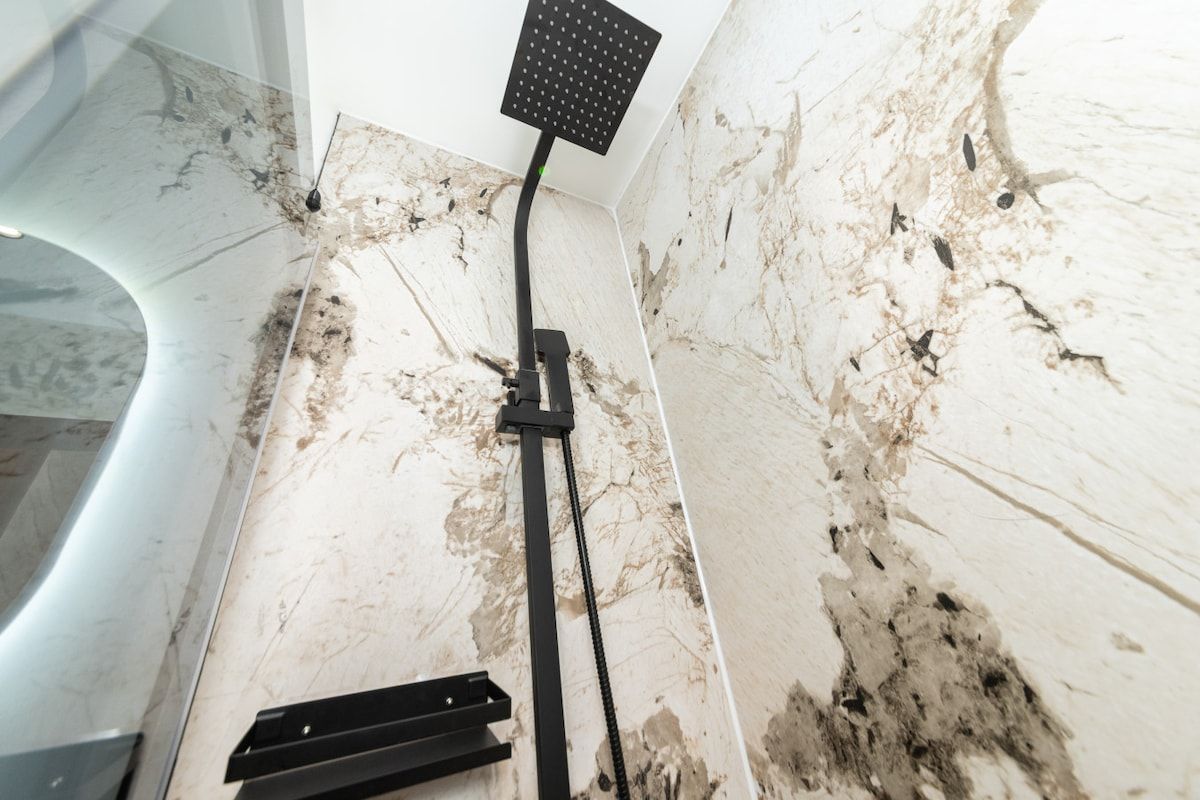 A shower with a handheld showerhead, a control panel, and a wall-mounted faucet.