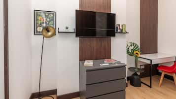 A modern room with a flat-screen TV mounted on the wall, a desk with a chair, a small plant, and a bookshelf.