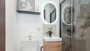 Une salle de bain moderne avec un lavabo blanc, un meuble-lavabo en bois et une cabine de douche en verre.