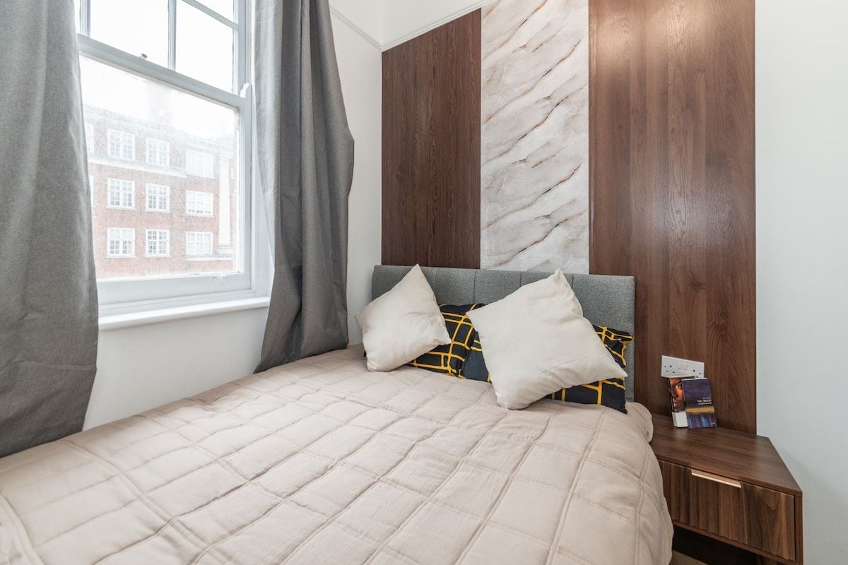 A bedroom with a bed, pillows, a nightstand, and a window.