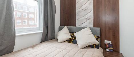 A bedroom with a bed, pillows, a nightstand, and a window.