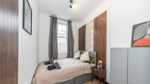 Une chambre à coucher avec un lit, une table de chevet, une armoire et une fenêtre avec des rideaux.