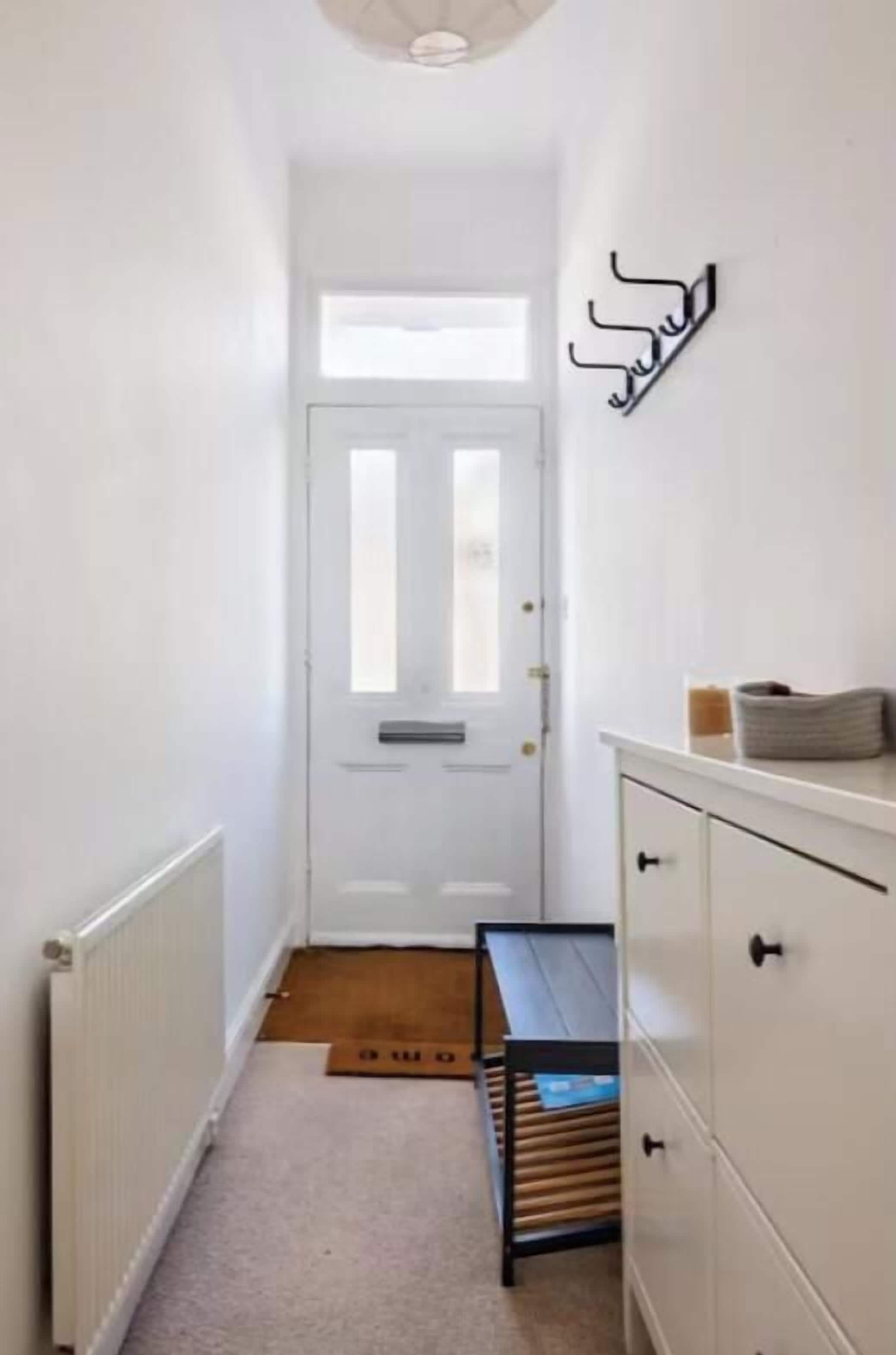 A narrow hallway with a white door, a radiator, a bench, and a white cabinet with drawers.