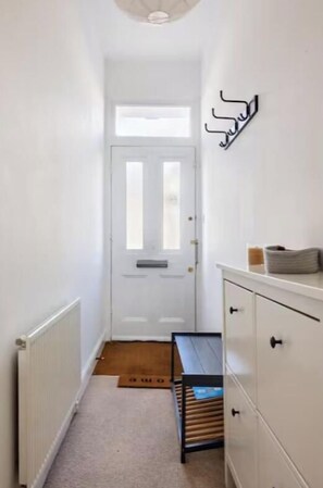 A narrow hallway with a white door, a radiator, a bench, and a white cabinet with drawers. - Bright Maida Vale Flat near Shops &Transport Links (London)