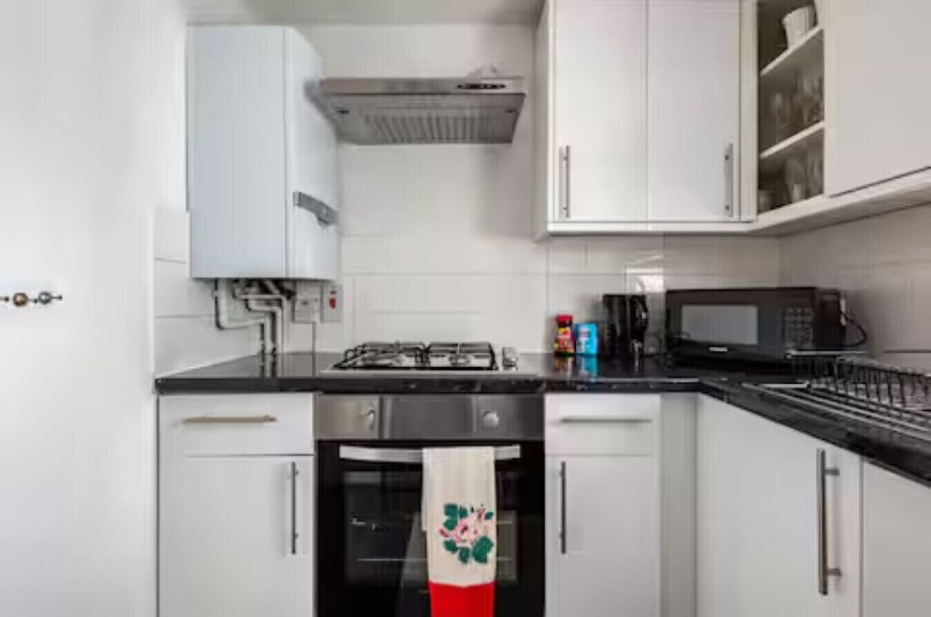 Une cuisine avec des meubles blancs, une cuisinière, un four à micro-ondes et un dosseret carrelé.