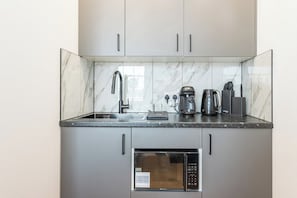A compact kitchen with a built-in microwave, a coffee maker, and a kettle on the countertop. - Prism Kensington - New Studio - Airconditioned (Greater London)