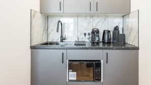 A compact kitchen with a built-in microwave, a coffee maker, and a kettle on the countertop. - New Kensington High Street Studio with AC (Greater London)