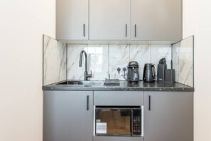 A compact kitchen with a built-in microwave, a coffee maker, and a kettle on the countertop. - New Kensington High Street Studio with AC (Greater London)