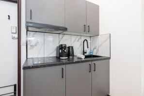 A compact kitchen with a built-in coffee maker, a sink, and a modern stove hood. - Lumen Kensington - Brand New - Airconditioned - W8 (Greater London)