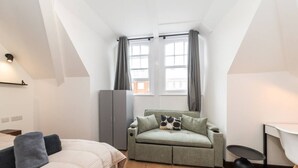 A compact room with a bed, a sofa, a small table, and a wardrobe. - Stylish New Studio in Kensington with AC (Greater London)