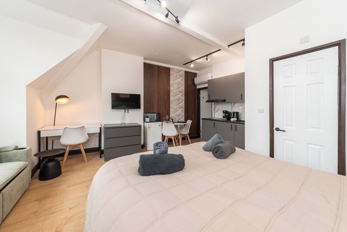 Een moderne slaapkamer met een groot bed, een bureau, een stoel en een kitchenette.