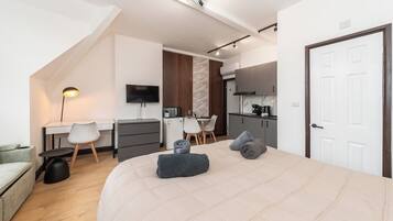 A modern bedroom with a large bed, a desk, a chair, and a kitchenette.