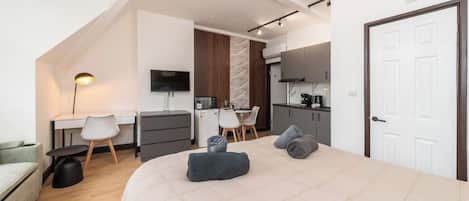 Een moderne slaapkamer met een groot bed, een bureau, een stoel en een kitchenette.