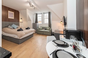 Une chambre moderne avec un lit, un canapé, une table à manger dressée pour deux personnes et un téléviseur.
