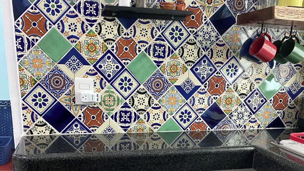 Une cuisine avec un mur recouvert de carreaux colorés, deux tabourets et un plan de travail.