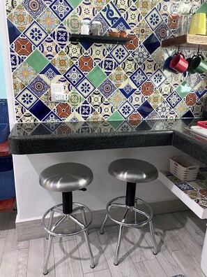 A kitchen with a colorful tile backsplash, two stools, and a countertop. - Centrally located walking distance from restaurants, Mercadito, etc... (Isla Mujeres)
