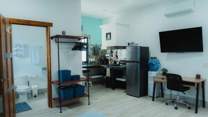 Un espace de vie compact comprenant un coin cuisine, un téléviseur fixé au mur et un bureau avec une chaise.