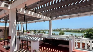 Un espace extérieur abrité comprenant une balançoire, un banc et une vue sur une rivière et le paysage urbain.
