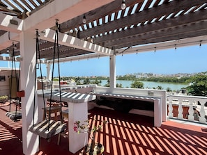 A covered outdoor area with a swing set, a bench, and a view of a river and cityscape. - Centrally located walking distance from restaurants, Mercadito, etc... (Isla Mujeres)
