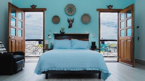 Une chambre à coucher avec un lit, une porte-fenêtre donnant sur un balcon et des éléments décoratifs accrochés au mur.