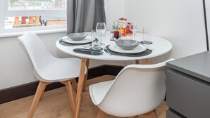 En matplats med ett runt bord, vita stolar och ett fönster med utsikt över byggnader.
