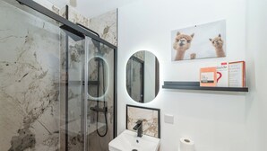 Ett modernt badrum med en duschkabin i glas, ett handfat med en väggbeklädnad i marmor och en toalett med en vit cistern.