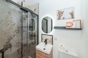 Une salle de bain moderne avec une douche à parois de verre, un lavabo avec un pare-éclaboussures en marbre et des toilettes avec une cuvette blanche.