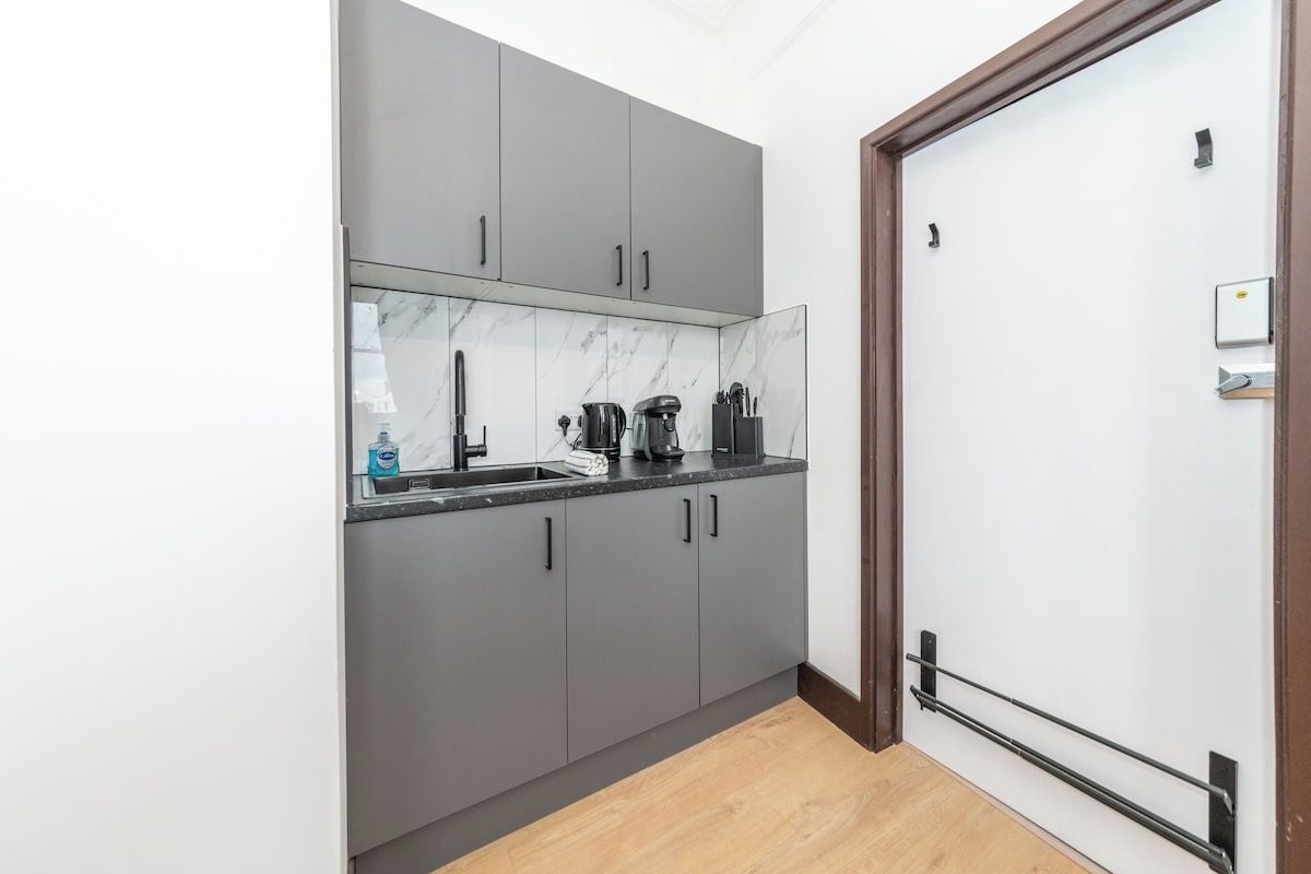 A kitchen with grey cabinets, a marble backsplash, a black countertop, and a wooden floor.