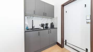 A kitchen with grey cabinets, a marble backsplash, a black countertop, and a wooden floor.