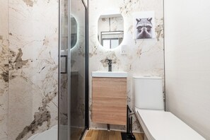 Une salle de bain avec une douche à parois de verre, un lavabo blanc, un meuble-lavabo en bois et des toilettes.