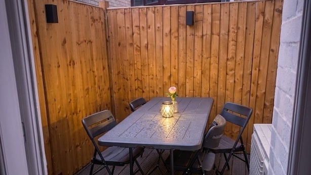 En träaltan med ett bord och stolar, en blomvas och en mur av tegelsten.