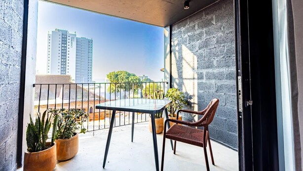 Un balcón con una mesa y sillas, plantas en macetas y vistas de edificios altos.
