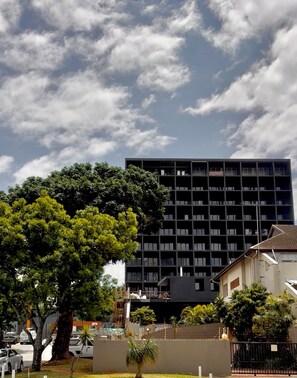 A modern building with a grid-like facade, surrounded by greenery and parked cars. - Blackbrick Hotel Umhlanga (uMhlanga)