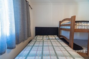 A single bed with a checkered bedspread, a wooden headboard, and a curtain partially drawn to the side. - Apt with Balcony & Parking 300m | Vila Tupi Beach (Praia Grande)