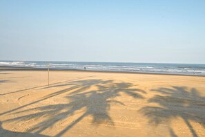 A beach with a sandy shore, palm tree shadows, and the ocean in the background. - Apt with Balcony & Parking 300m | Vila Tupi Beach (Praia Grande)