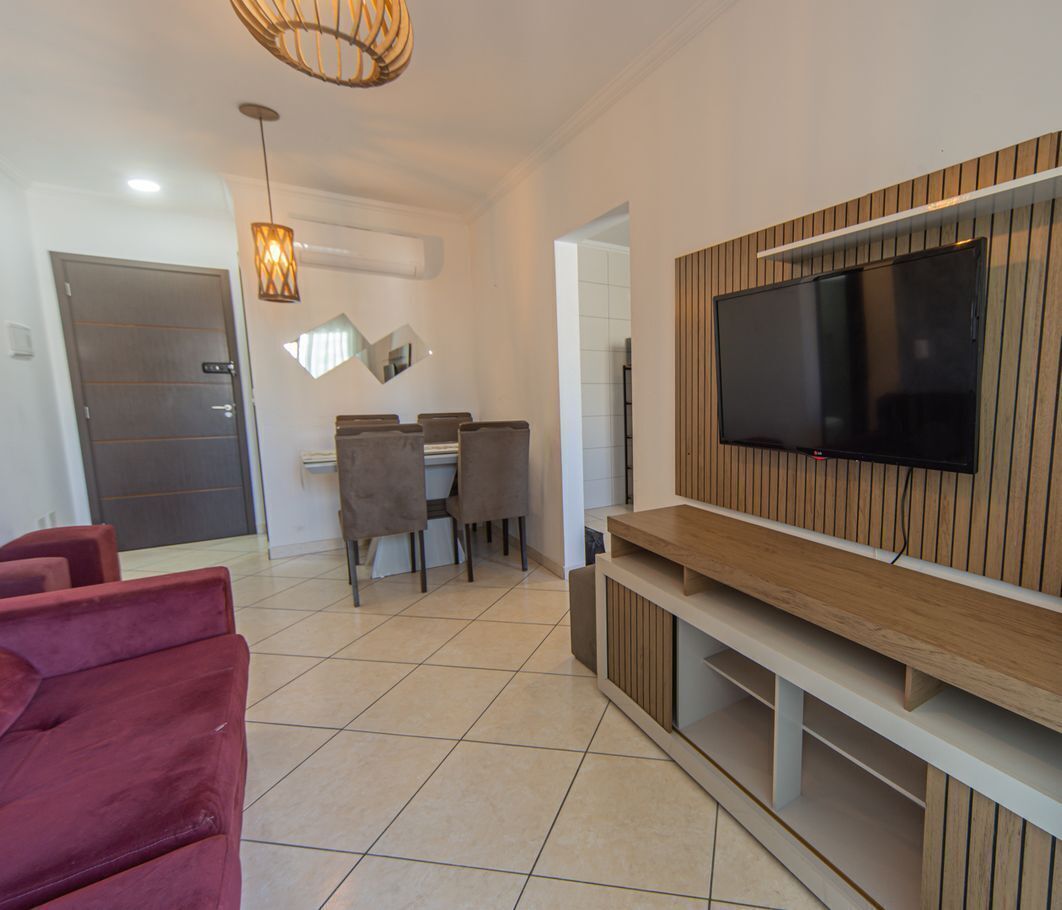 Ein modernes Wohnzimmer mit Flachbildfernseher an einer Wand aus Holzpaneelen, einem Essbereich mit Tisch und Stühlen sowie einem roten Sofa.