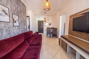Ein Wohnzimmer mit einem roten Sofa, einem Holzboden-TV-Schrank und einem Essbereich mit Stühlen.
