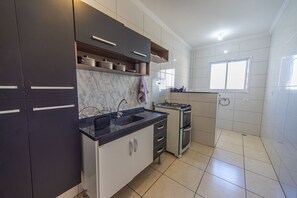 A modern kitchen with dark cabinets, a marble countertop, and a built-in stove. - Apt with Balcony & Parking 300m | Vila Tupi Beach (Praia Grande)