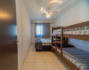 Ein kleiner, kompakter Raum mit einem Etagenbett, einem Einzelbett, einem Deckenventilator und einem Fenster mit Vorhängen.