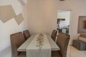 Un comedor con una mesa dispuesta para cuatro personas, rodeada de sillas, y una cocina visible al fondo.