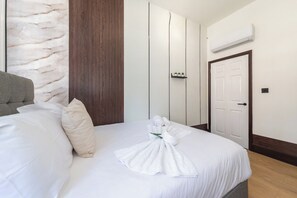 A hotel room with a bed, a wooden panel wall, a white door, and an air conditioning unit. - Halcyon Kensington 1 Bedroom - Airconditioned (Greater London)