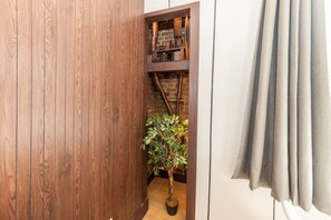 Ein schmaler Korridor mit Holzvertäfelung, einem Blumentopf und einem Blick auf eine Ziegelwand mit freiliegenden Rohren.