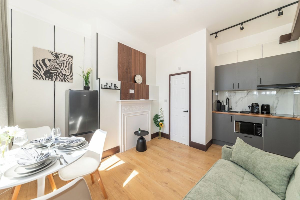 Una cocina moderna con horno empotrado y microondas, un comedor con mesa para cuatro, y una sala de estar con sofá.