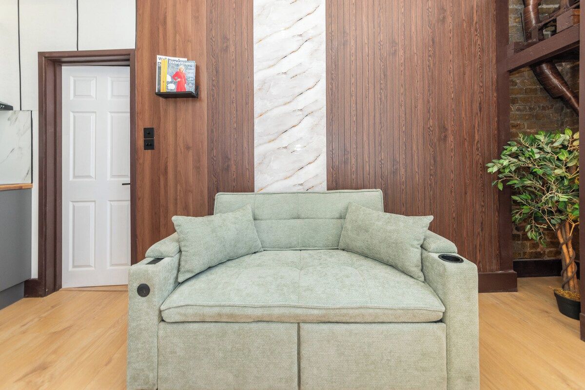 A corner sofa with a cushion, a door, a marble wall, and a plant.
