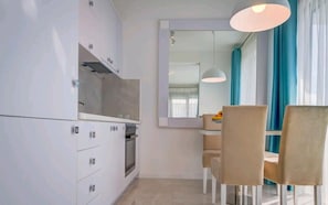 A modern kitchen with white cabinets, a built-in oven, and a dining area with a table and chairs. - Villa Blue Panorama 2 - Private Pool & Sea View in Budva (Budva)