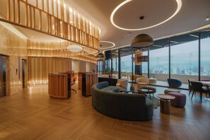 A modern interior with a wooden reception desk, seating area, and large windows offering a city view. - Centric & luxury suite w sauna, jacuzzi & gym (Mexico City)