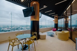 A modern lounge area with a glass wall, a round table with chairs, and a flat-screen TV mounted on a pillar. - Centric & luxury suite w sauna, jacuzzi & gym (Mexico City)