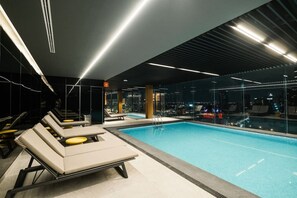 A modern indoor swimming pool with lounge chairs and a city view. - Centric & luxury suite w sauna, jacuzzi & gym (Mexico City)