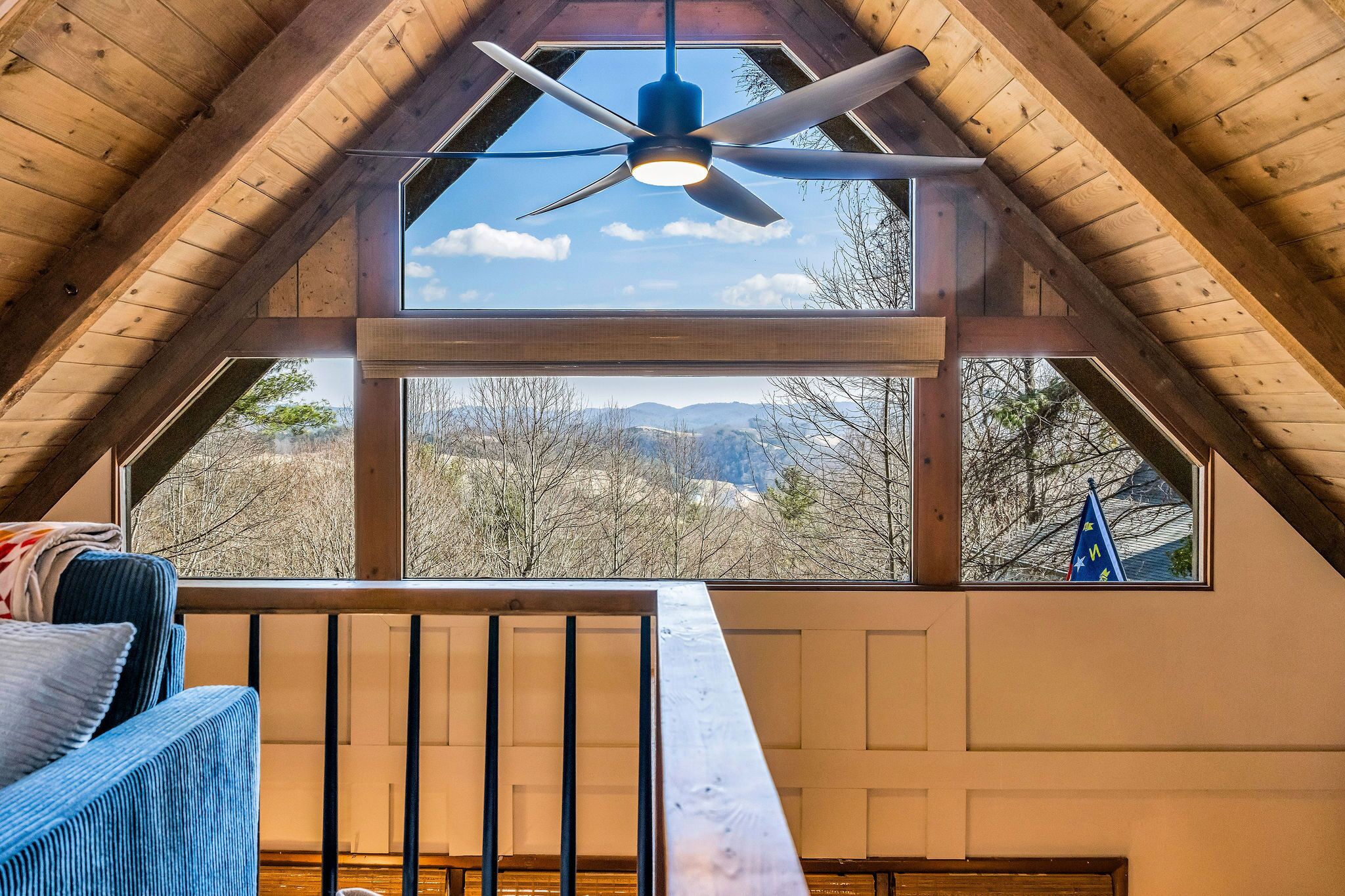 A room with a sloped ceiling, a ceiling fan, and large windows offering a view of trees and mountains.